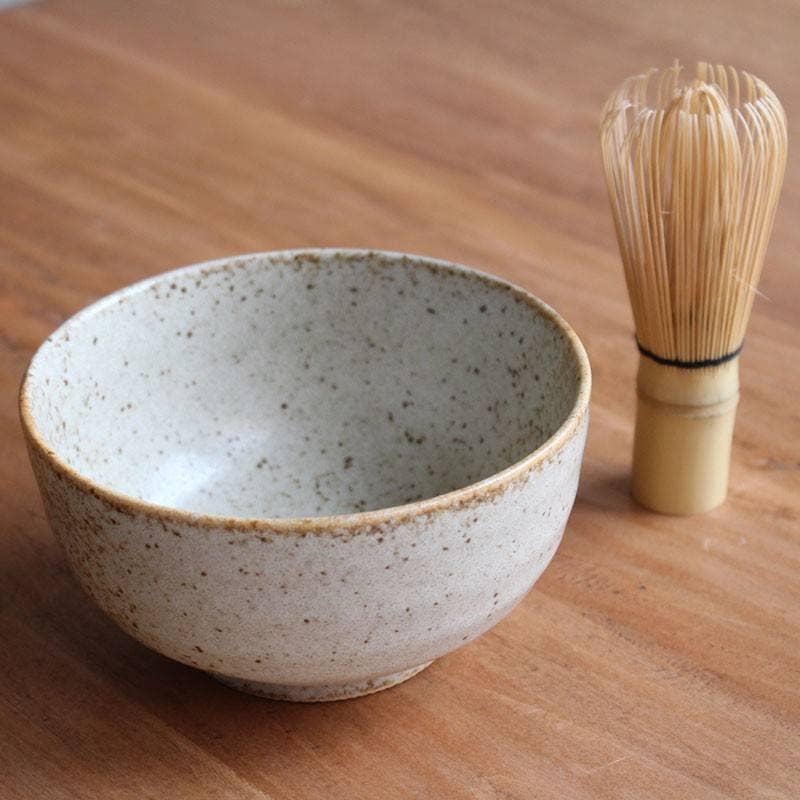 Ceramic bowl and bamboo whisk on a wooden surface