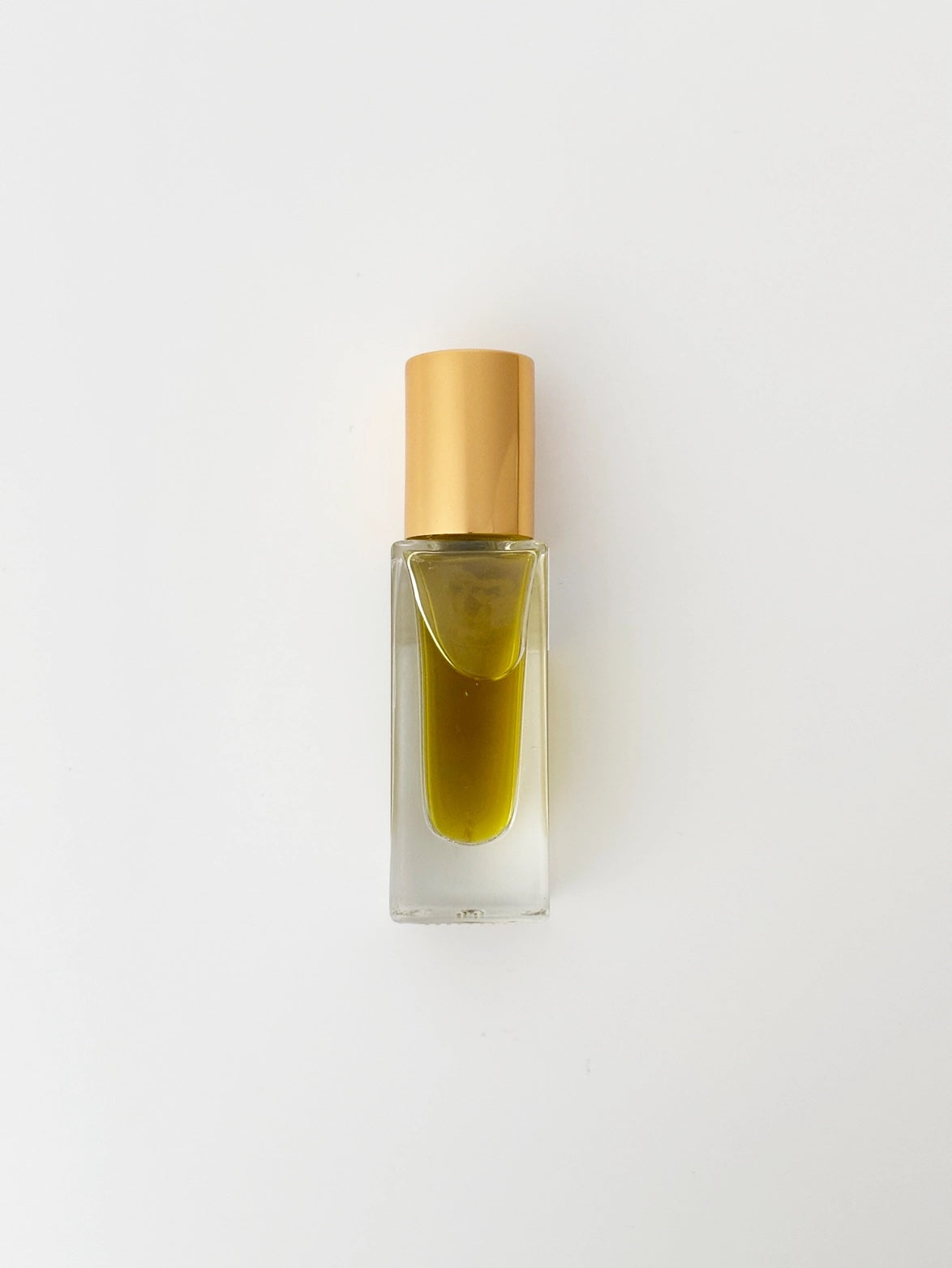 Small glass bottle with gold cap containing perfume on a light gray background