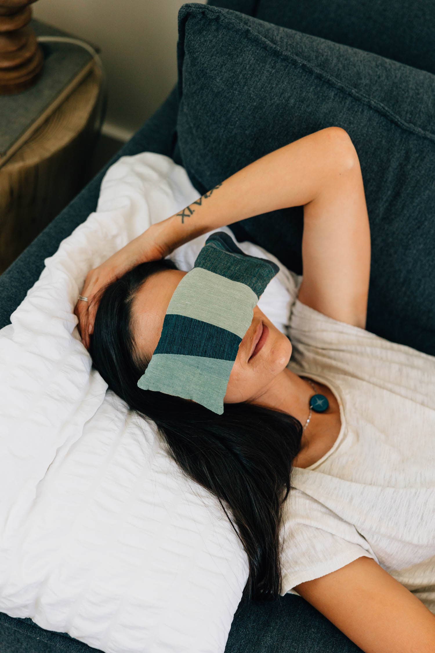 Woman lying on a couch with a green and black striped eye mask on her eyes.