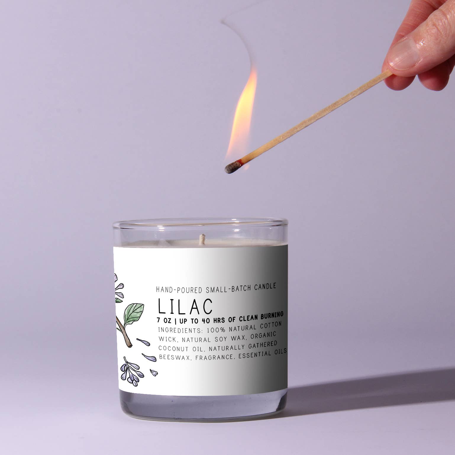 Candle labeled 'Lilac' being lit with a match against a light purple background
