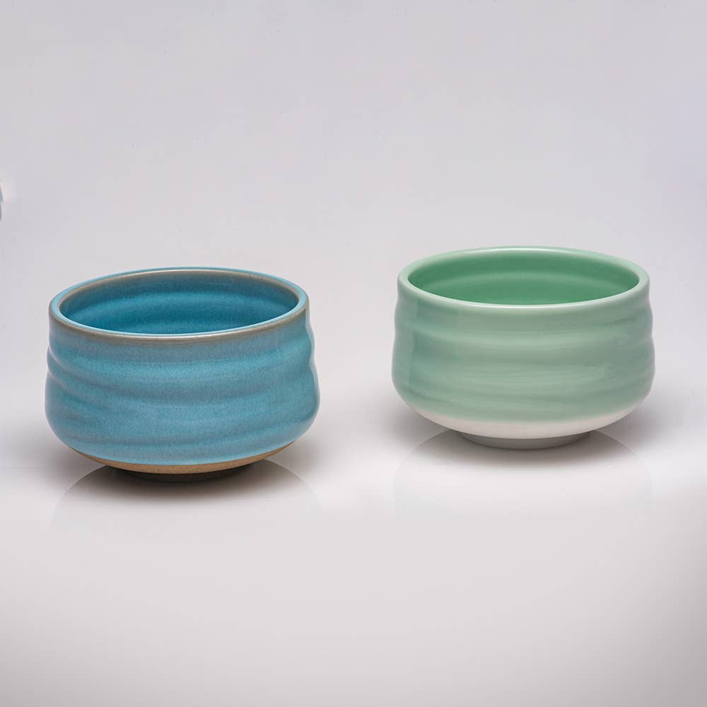 Two ceramic bowls, one blue and one green, on a white background
