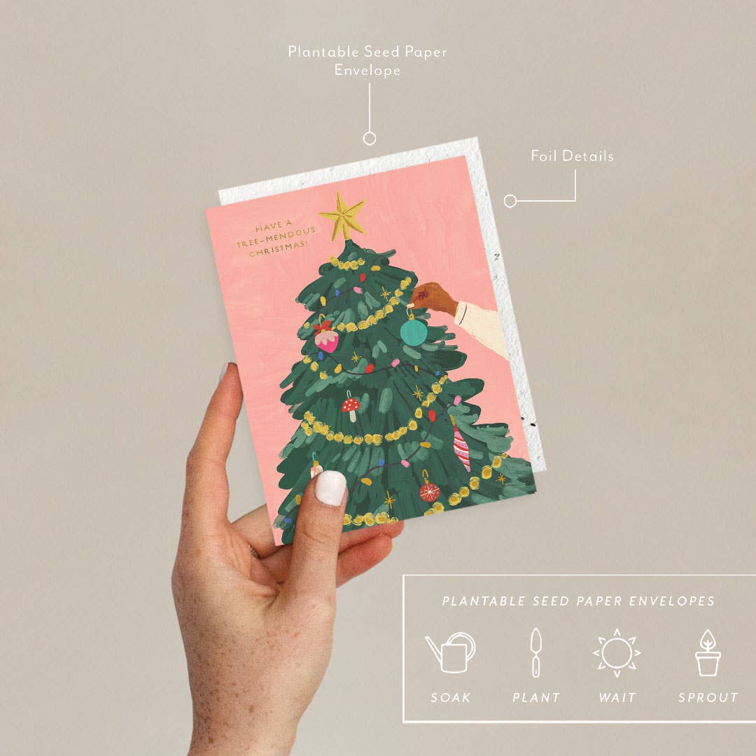 Hand holding a card with a Christmas tree design on a beige background.