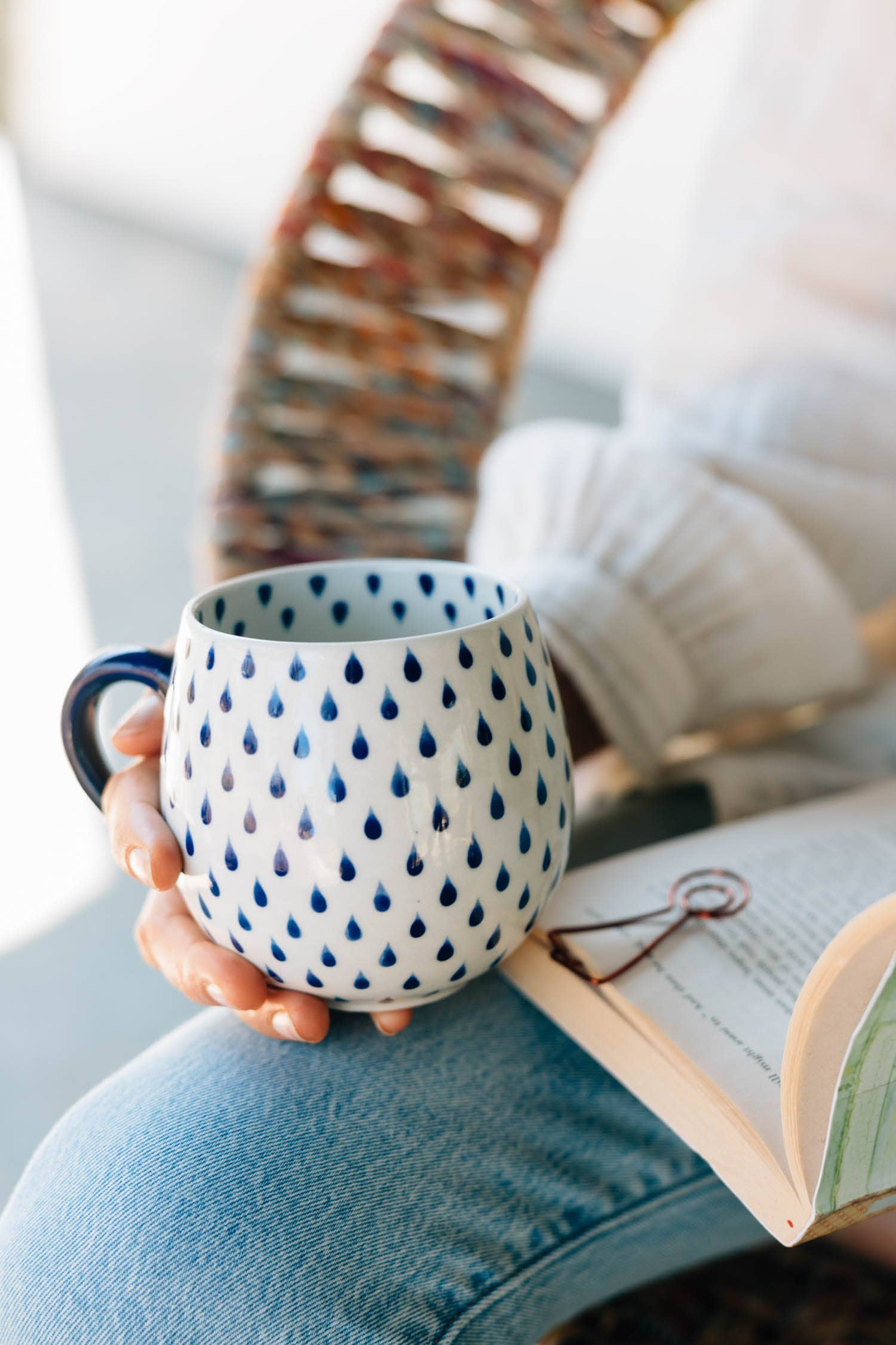 Person holding a mug with a blue pattern while reading a book indoors.