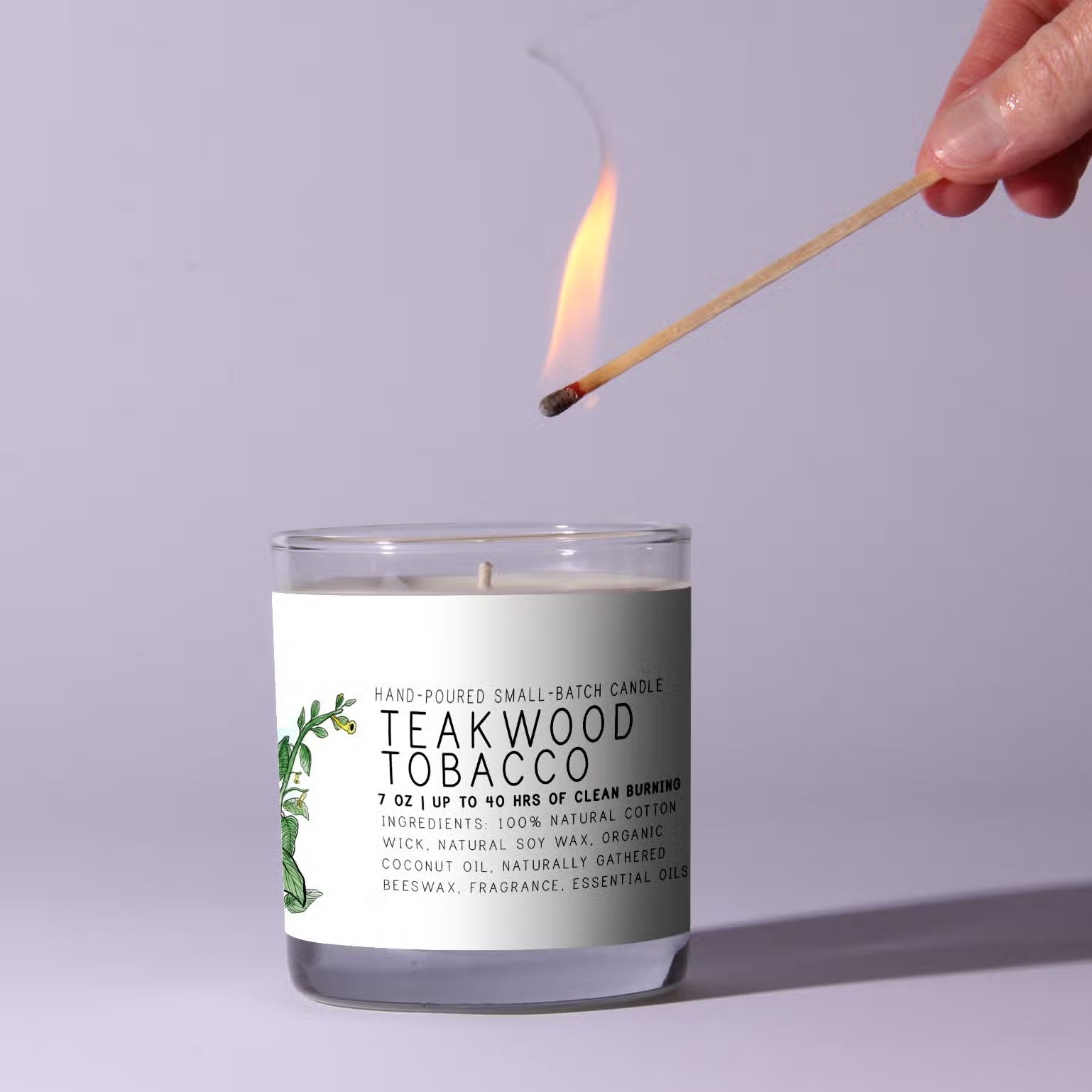 Candle labeled 'Teakwood Tobacco' being lit with a match against a light purple background