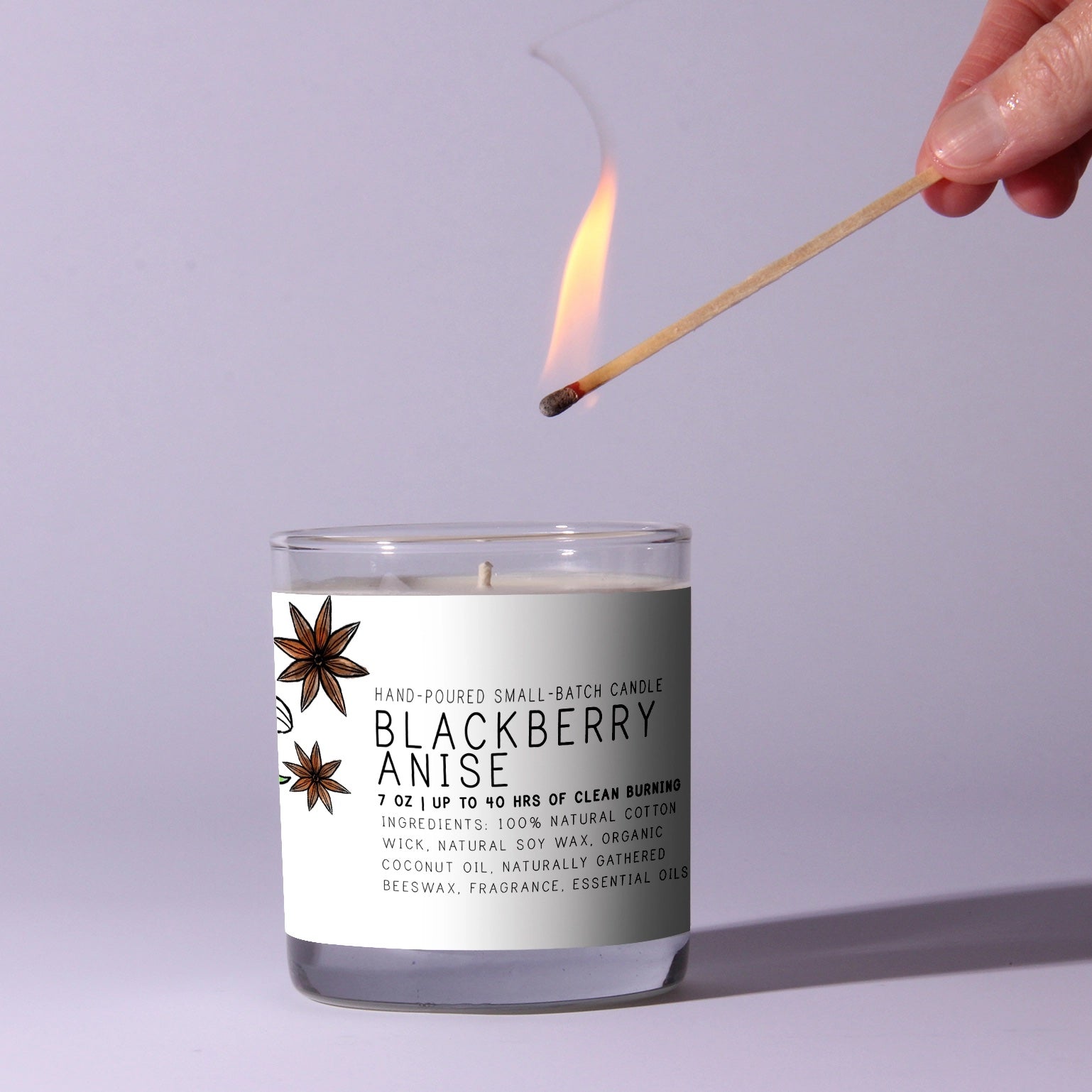 Candle labeled 'Blackberry Anise' being lit with a match against a light purple background