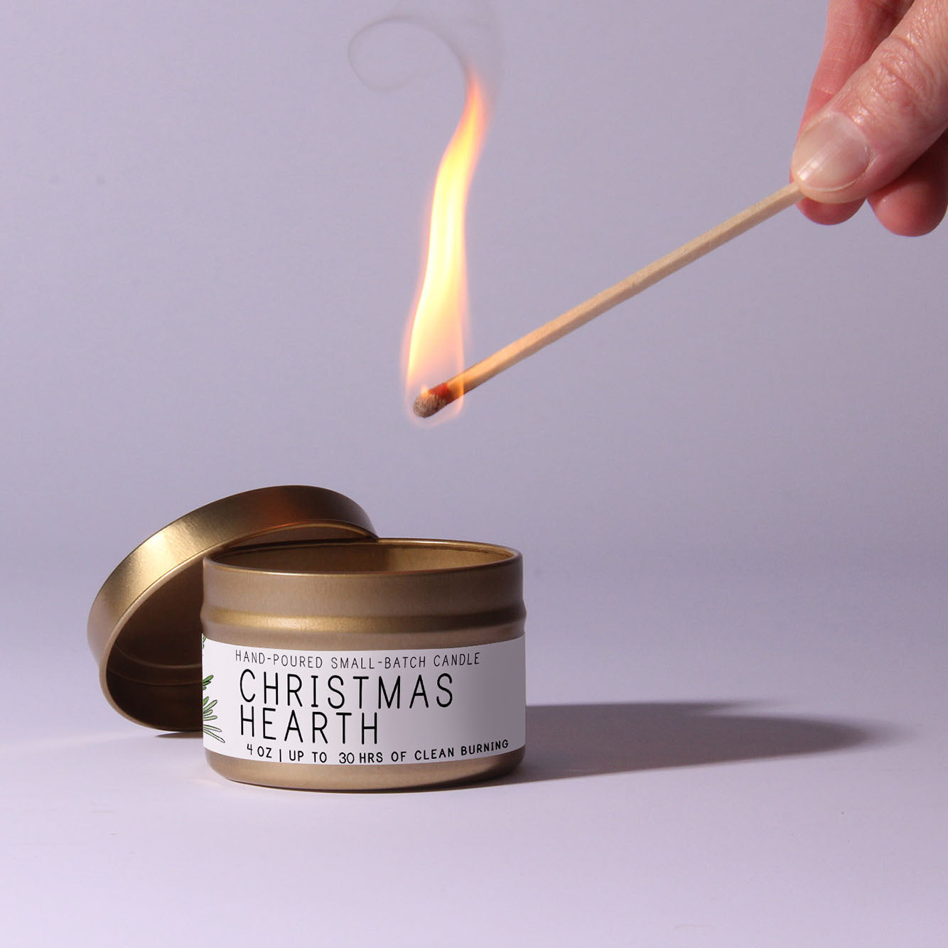 Candle labeled 'Christmas Hearth' being lit with a match on a light purple background