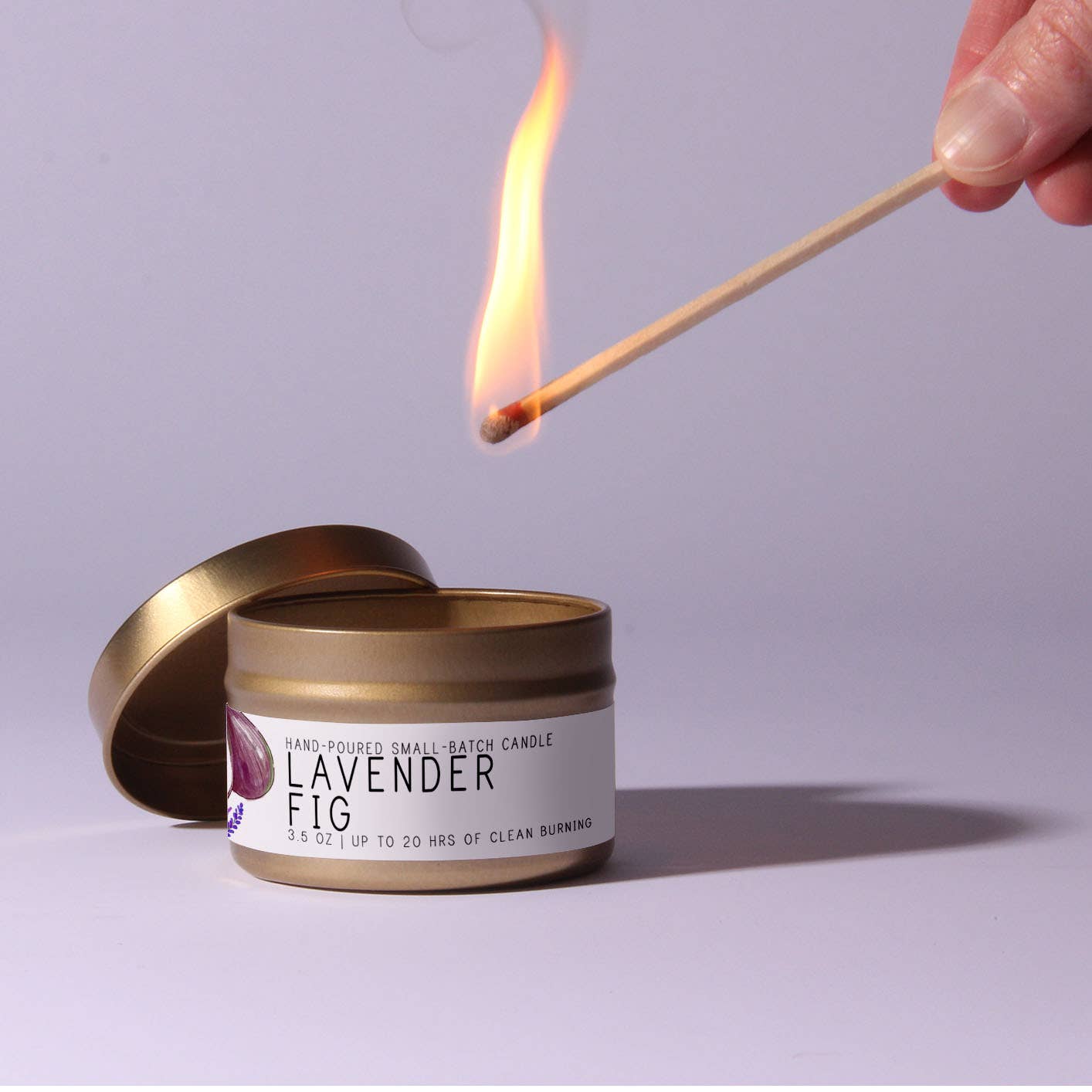 Candle labeled 'Lavender Fig' being lit with a match on a light purple background