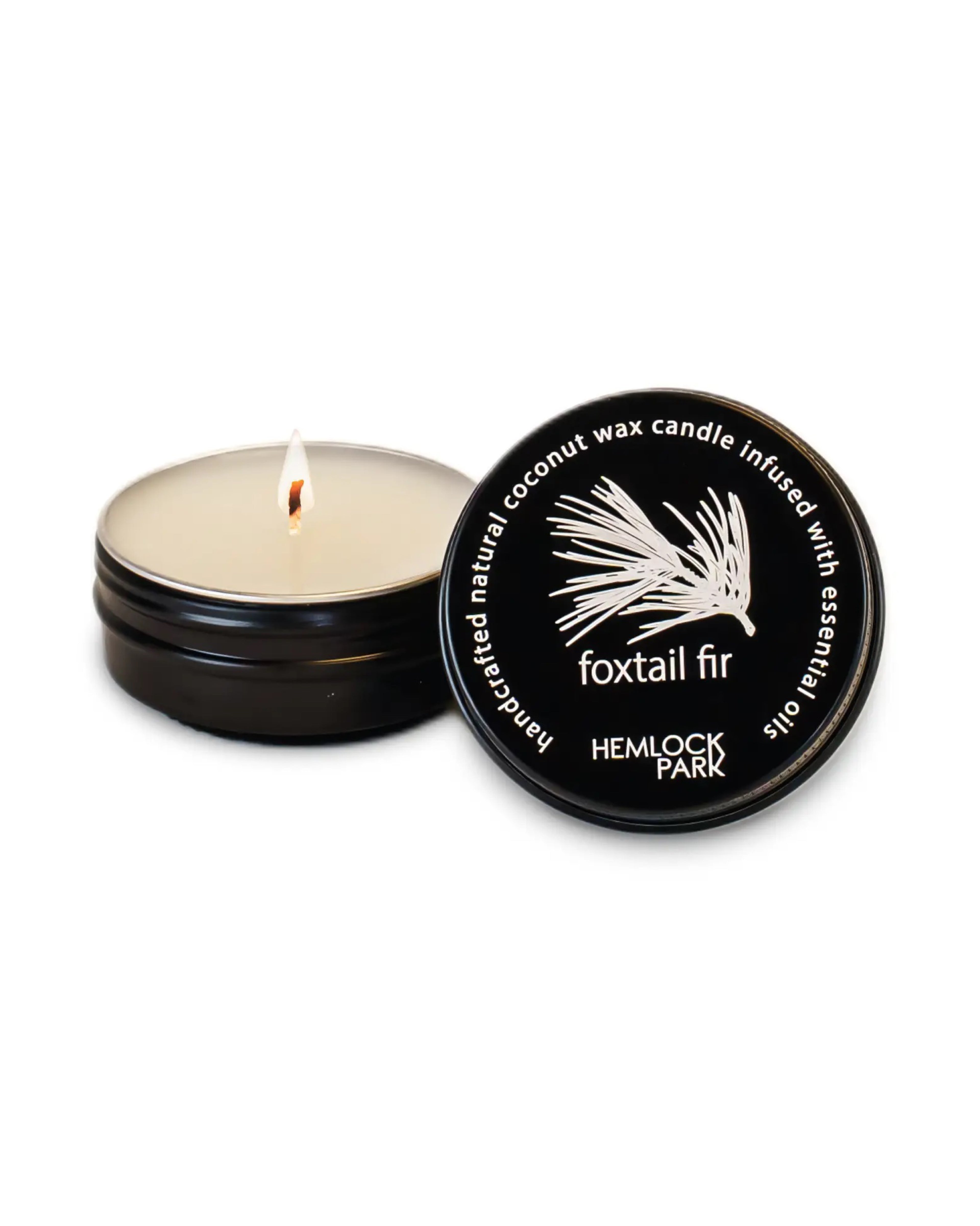 Hemlock Park candle with lit wick and black lid on a white background