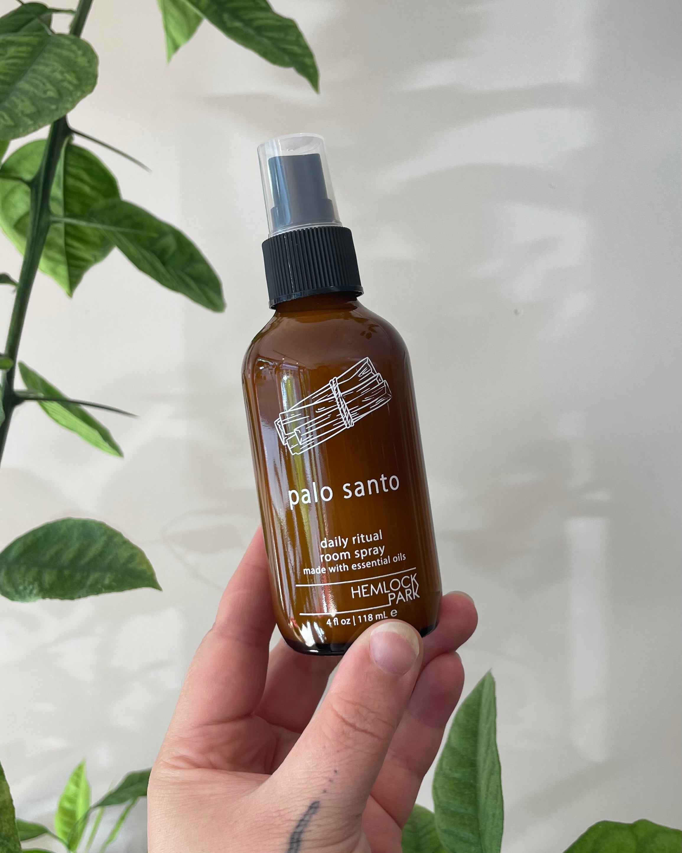 Hand holding a bottle of 'palo santo' room spray with green leaves in the background