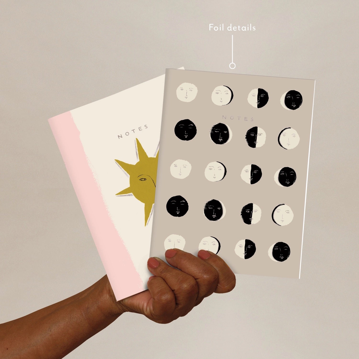 Hand holding a notebook with a sun illustration and a notebook with moon illustrations on a beige background