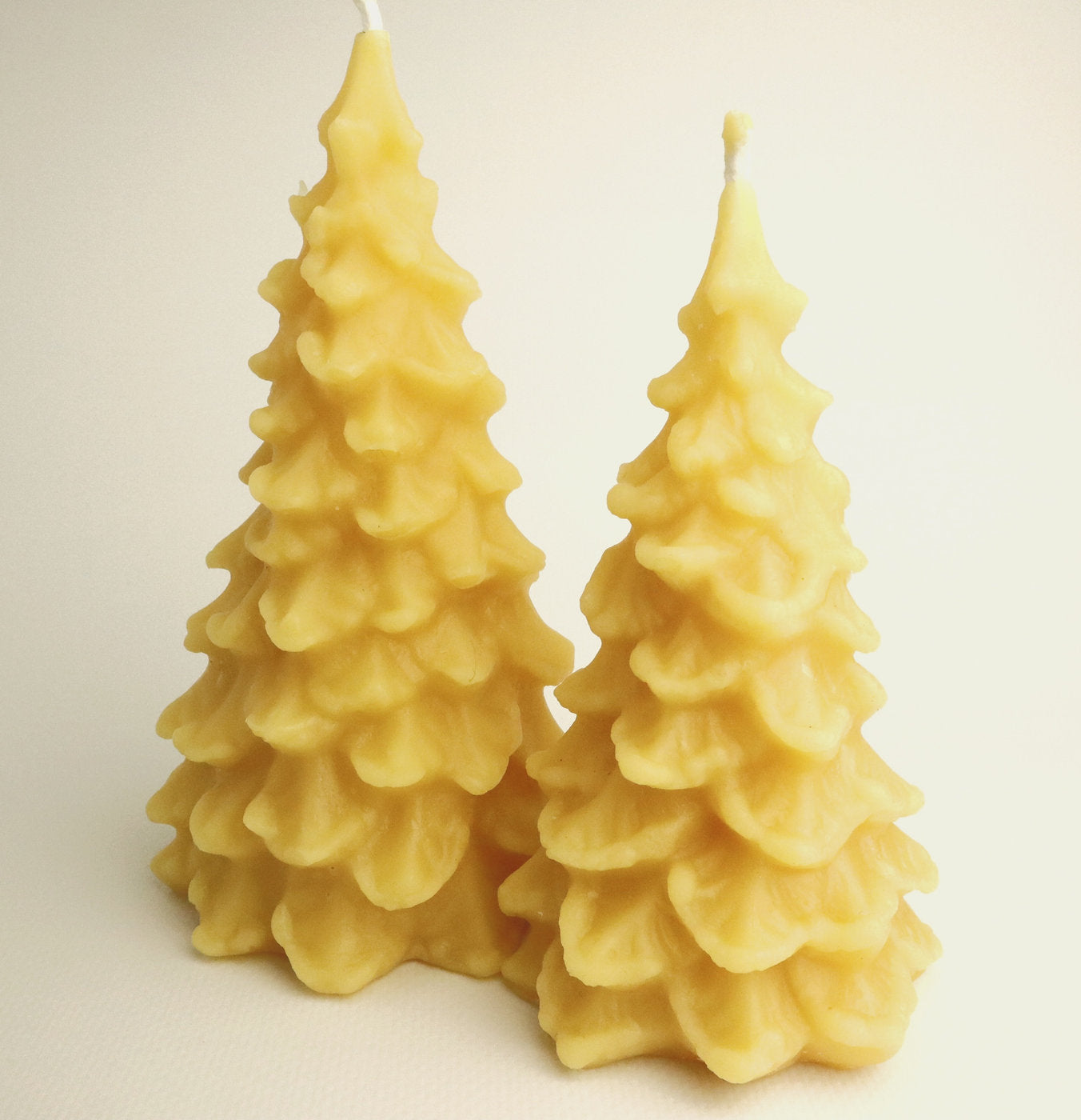 Two yellow tree-shaped candles on a light beige background
