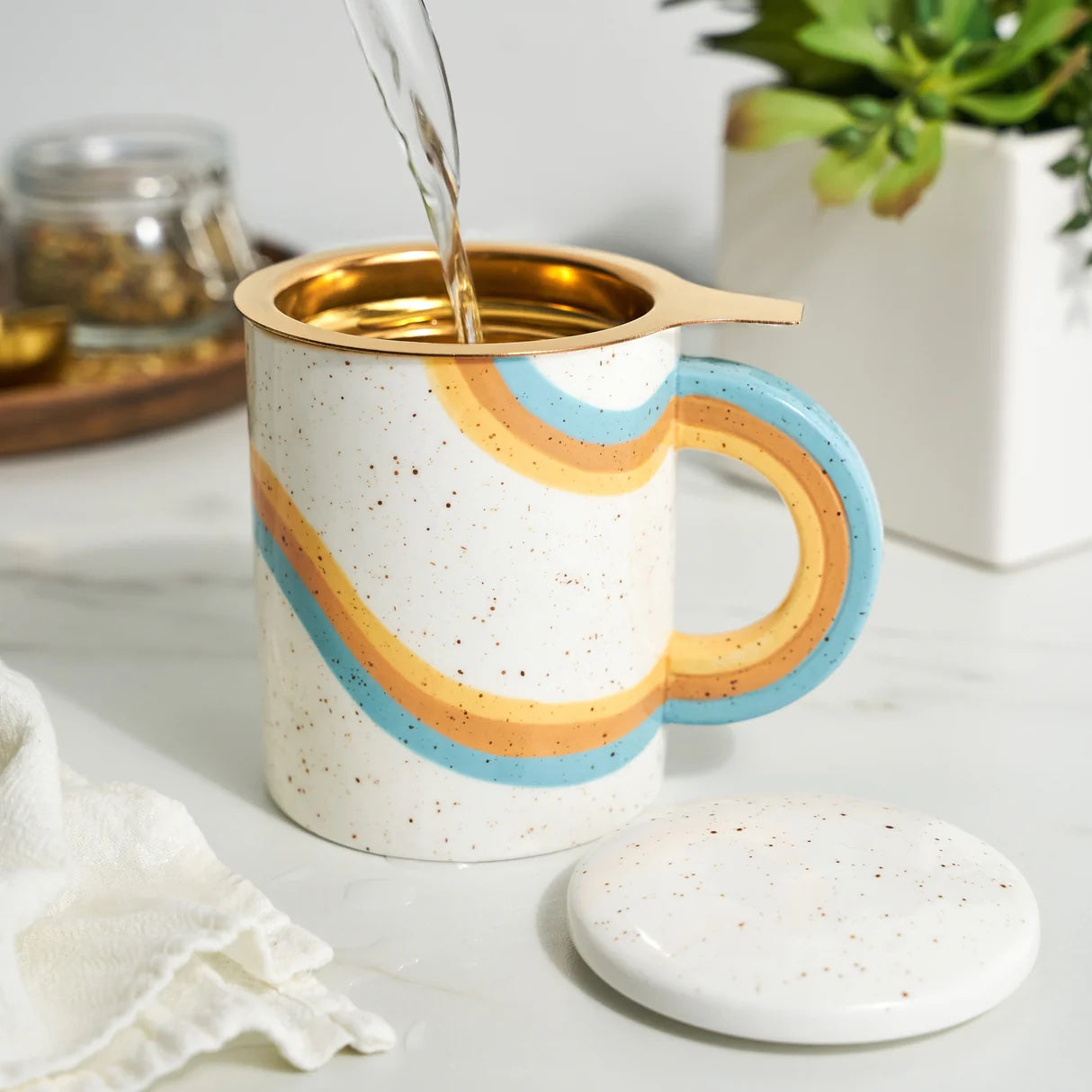Speckled ceramic mug with rainbow design being filled with a liquid, placed on a marble surface.