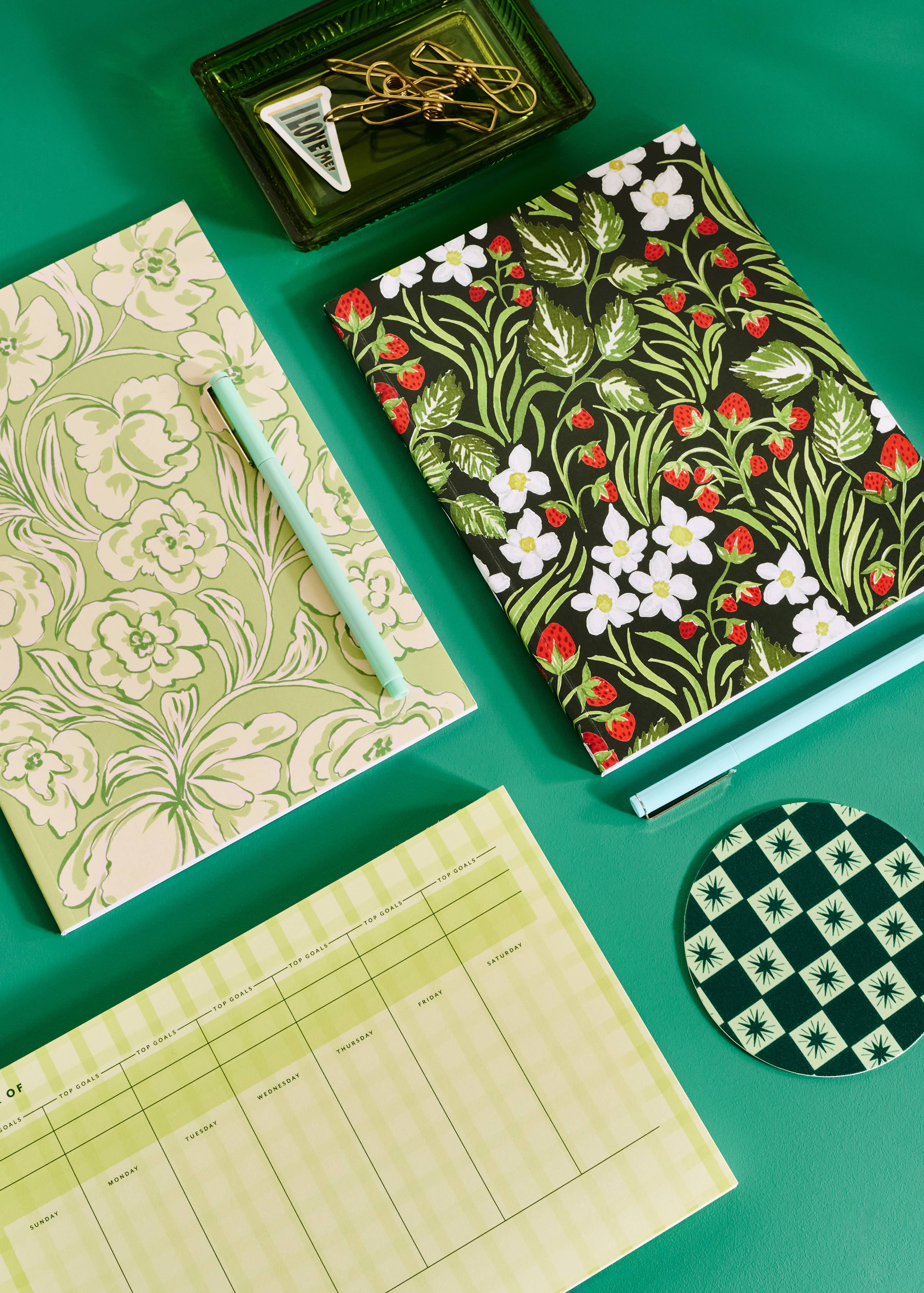 Stationery items including notebooks, a pen, and coasters on a green background