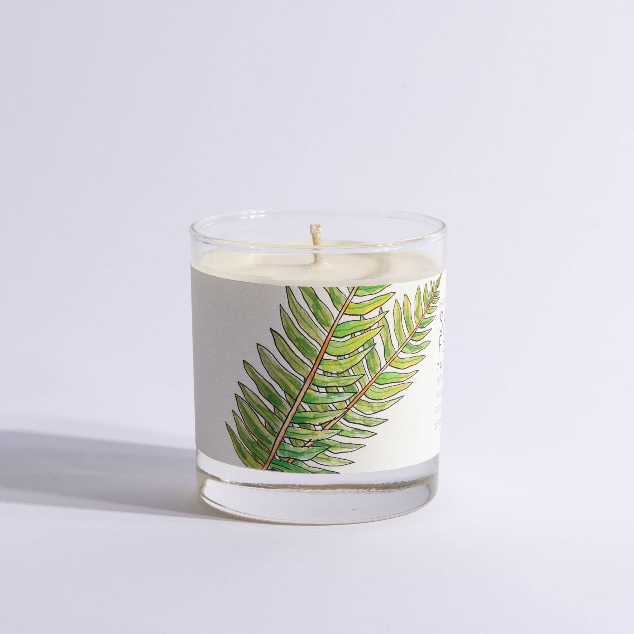 Candle in a glass jar with a fern leaf design on a light gray background