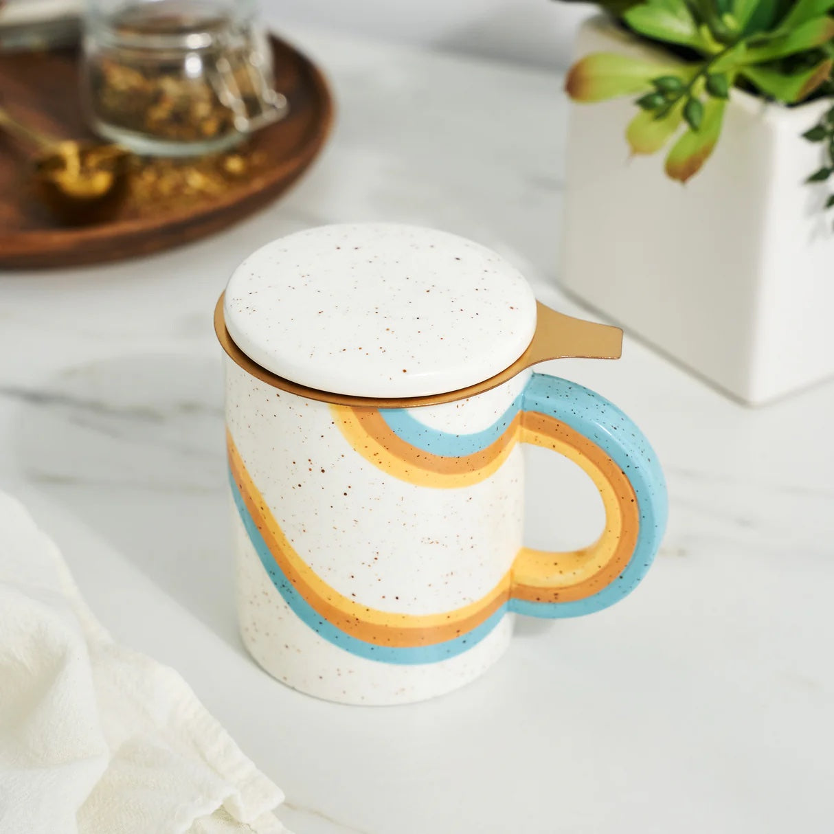 Speckled ceramic mug with colorful handle and lid on a marble surface.