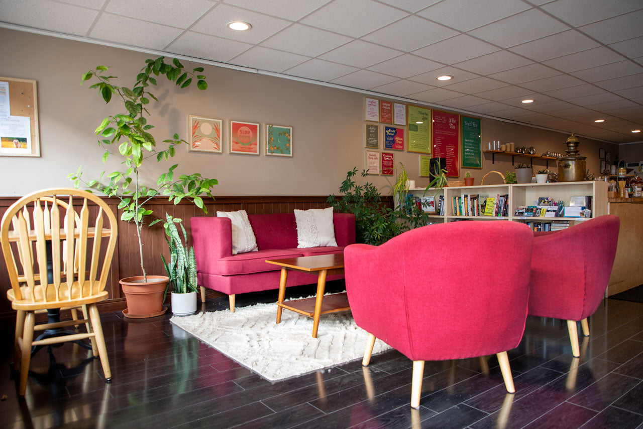 Lounge area with red chairs, wooden table, and plants in a well-lit room.
