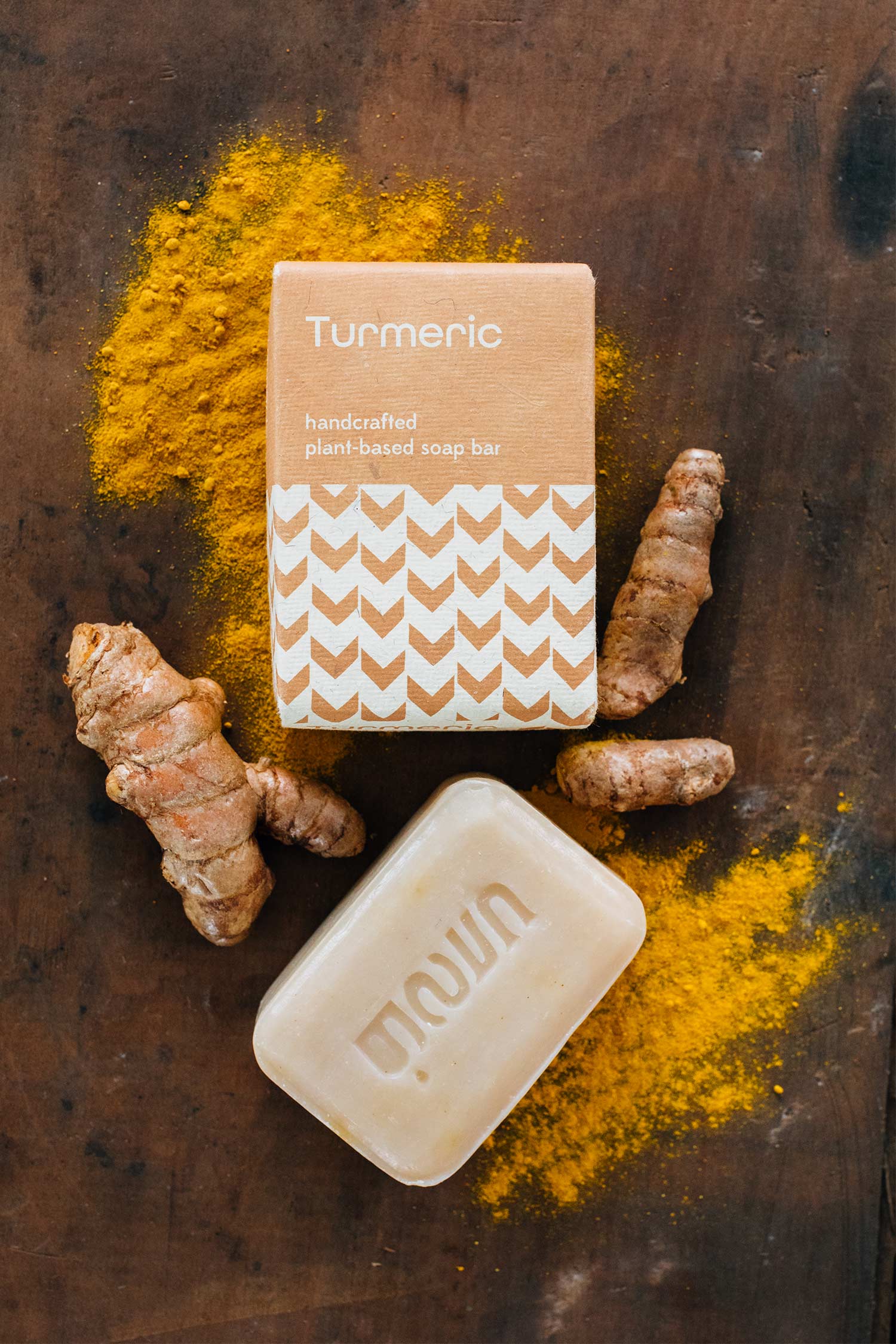 Turmeric soap bar with turmeric root and powder on a wooden surface