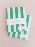 Two green and white striped notebooks on a beige background