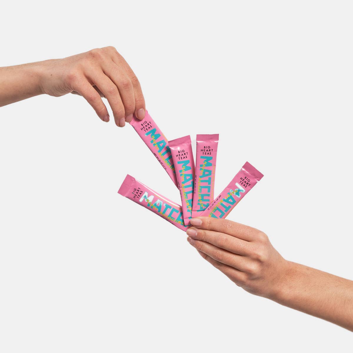 Two hands holding pink packets of matcha with colorful text on a light gray background