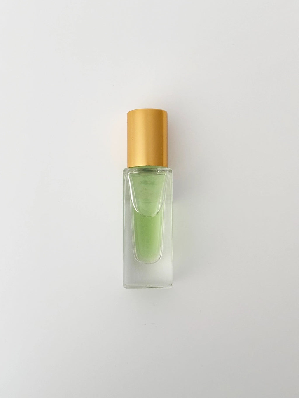 Small glass bottle with gold cap containing perfume on a light gray background