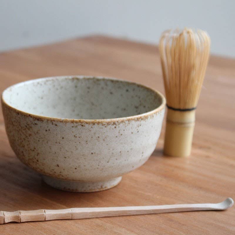 Ceramic bowl with wooden whisk and spoon on a wooden surface
