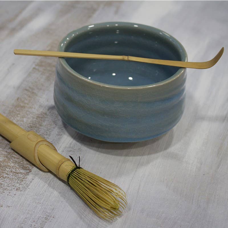 Blue ceramic bowl with a wooden whisk on a light wooden surface