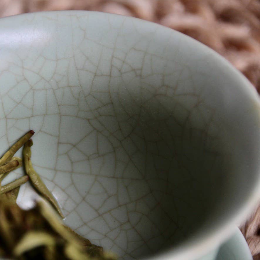 Close-up of a ceramic cup with a cracked glaze texture, featuring a tea leaf.