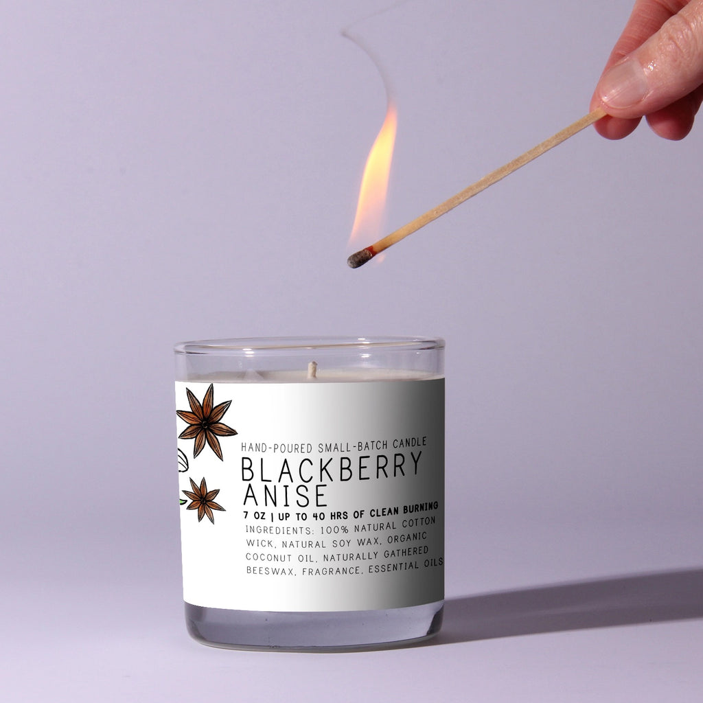 Candle labeled 'Blackberry Anise' being lit with a match against a light purple background