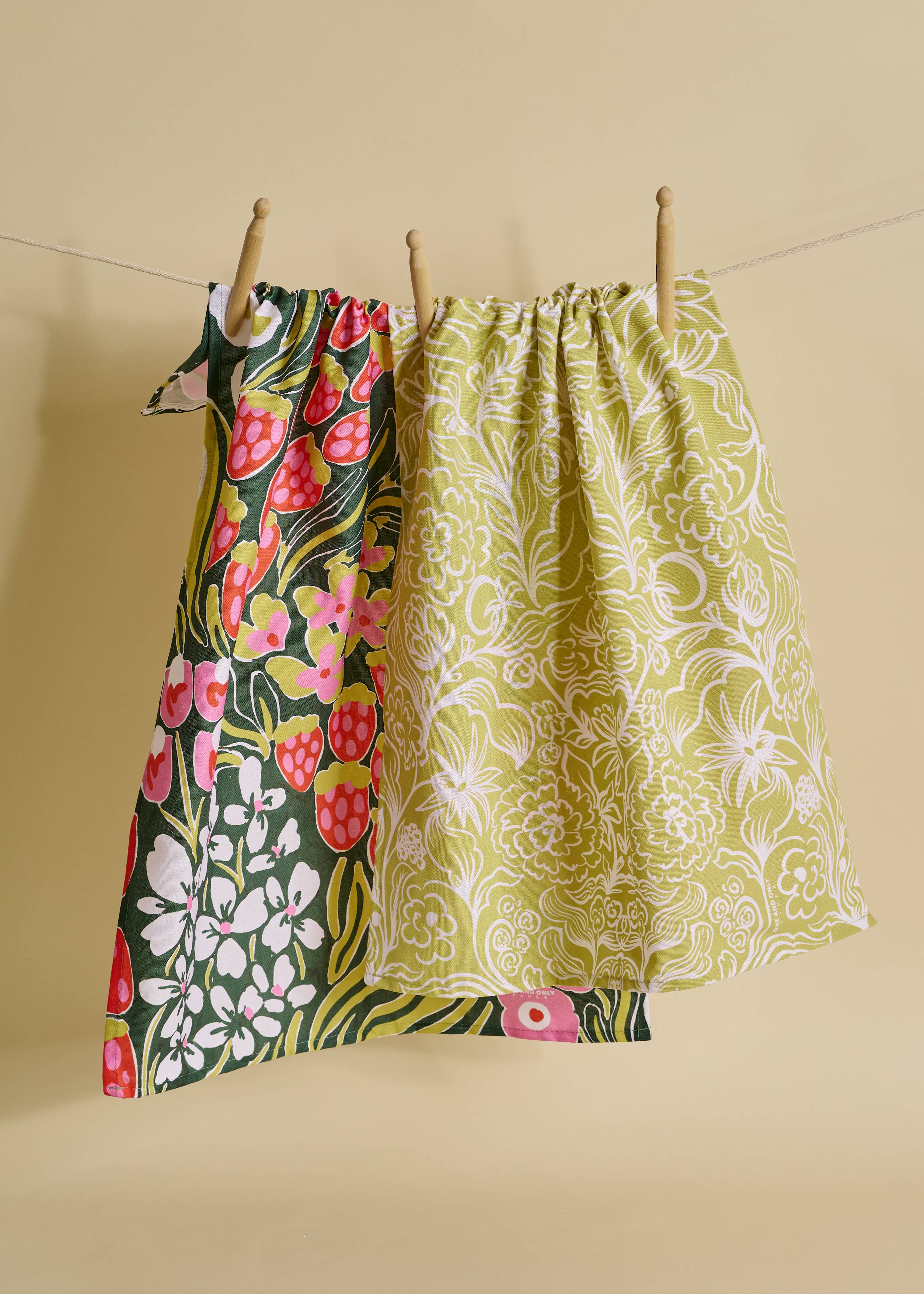 Two patterned tea towels hanging on a line against a beige background