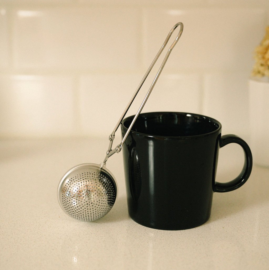 Black mug with a metal tea ball on a beige surface