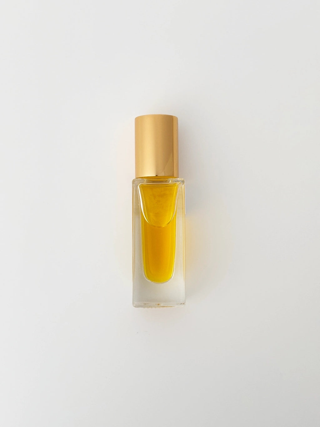 Small glass bottle with gold cap containing perfume on a light gray background