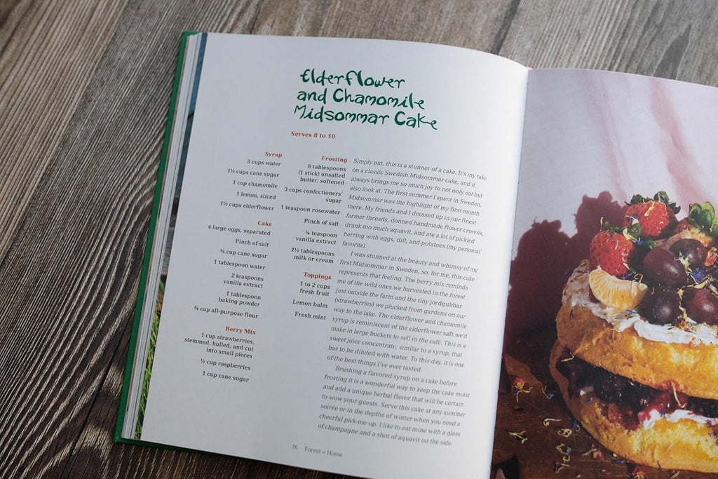 Open cookbook showing a recipe for a layered cake with strawberries and cherries on a wooden surface.