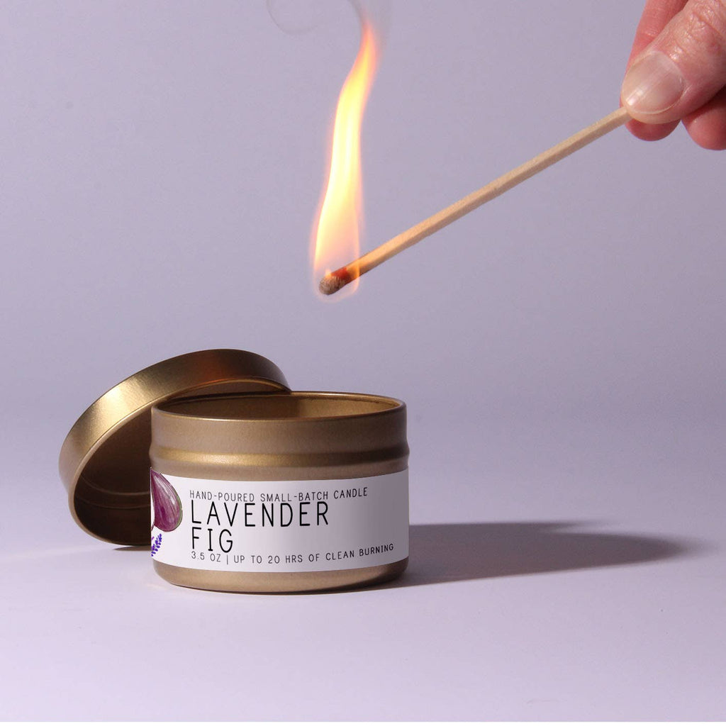 Candle labeled 'Lavender Fig' being lit with a match on a light purple background