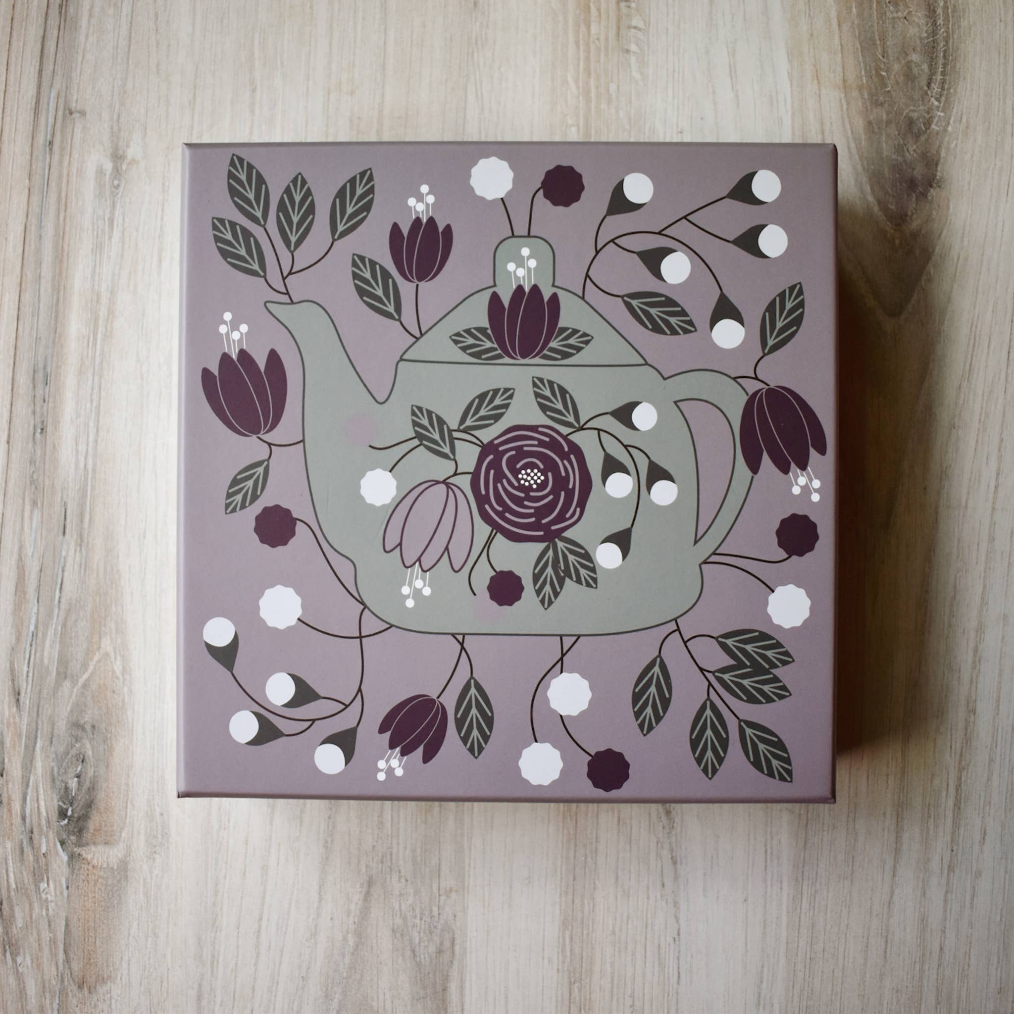 Decorative box with a teapot and floral design on a wooden surface