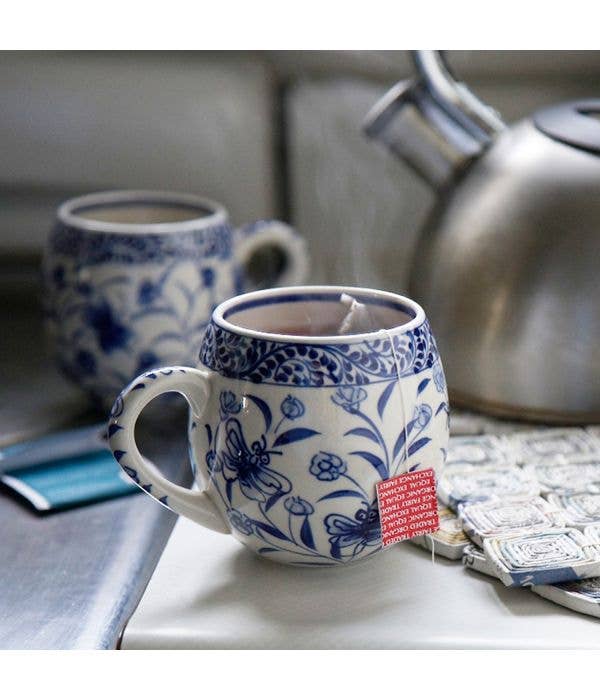 Blue and white patterned mug with a tea bag on a kitchen counter, next to a silver teapot.