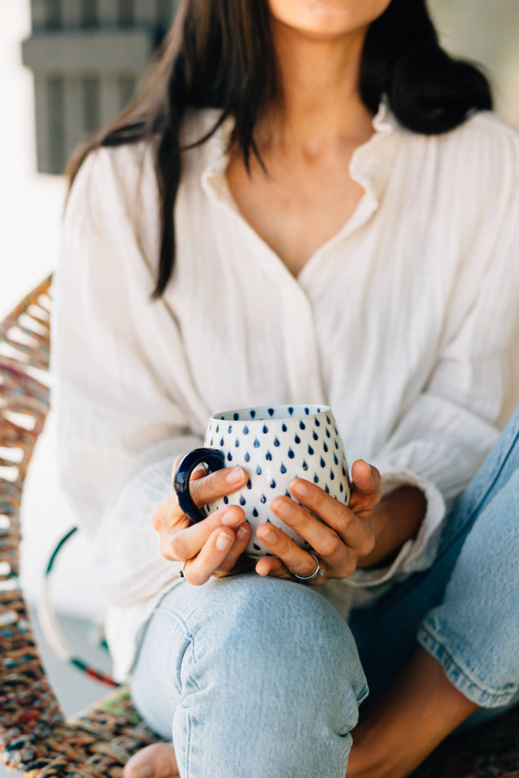 Person holding a ceramic mug with a pattern, wearing a white shirt and light blue jeans.