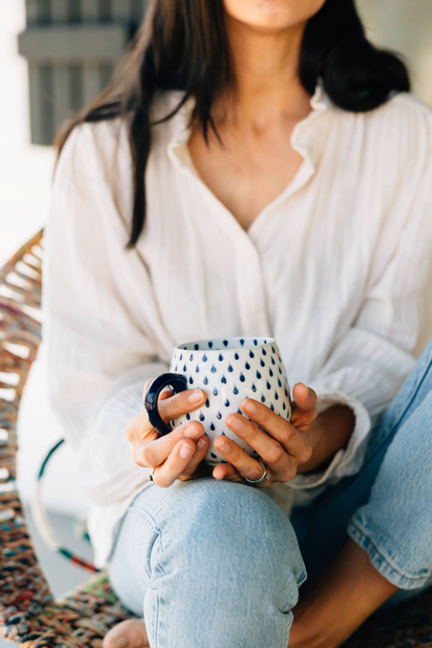 Person holding a ceramic mug with a pattern, wearing a white shirt and light blue jeans.