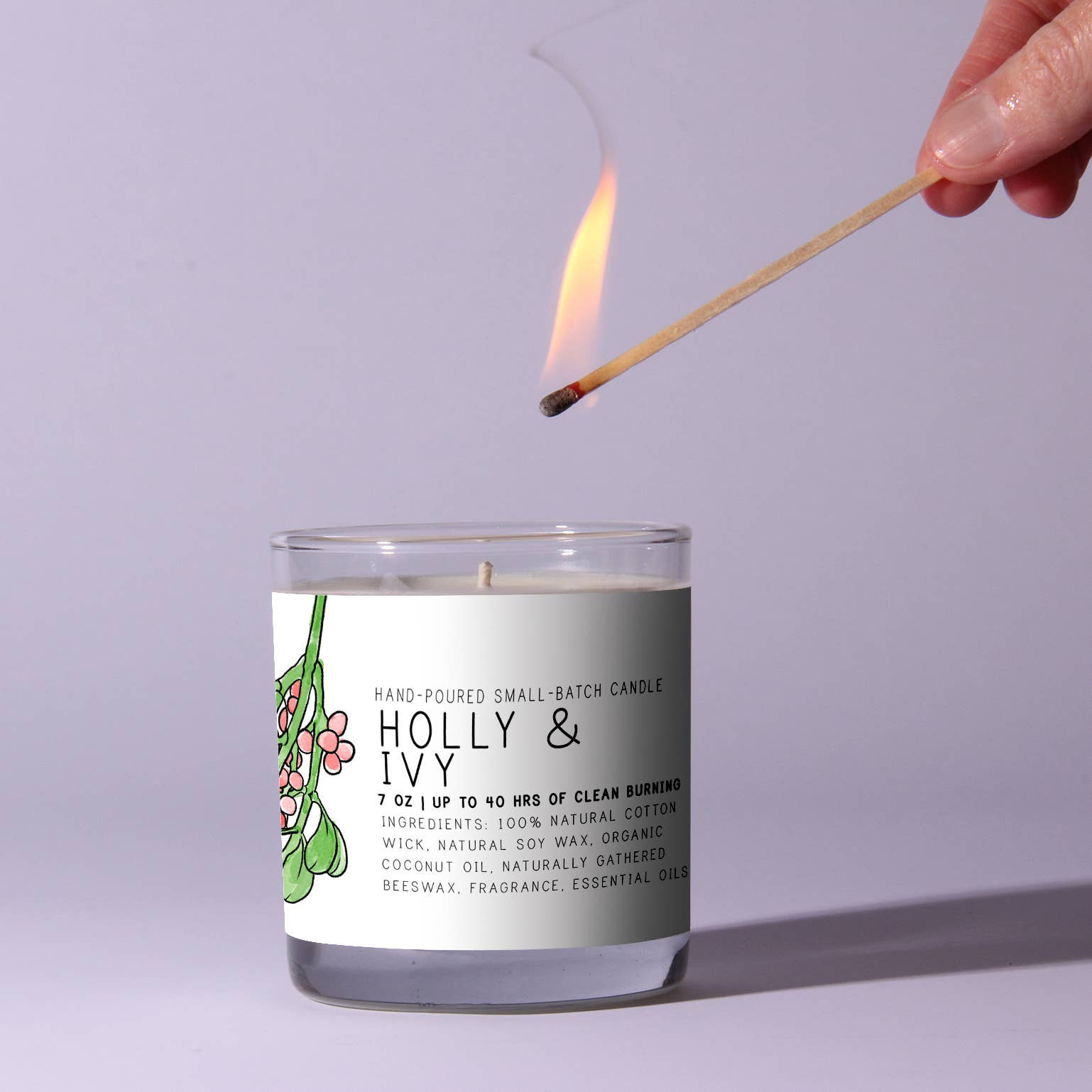 Candle labeled 'Holly & Ivy' being lit with a match on a light purple background