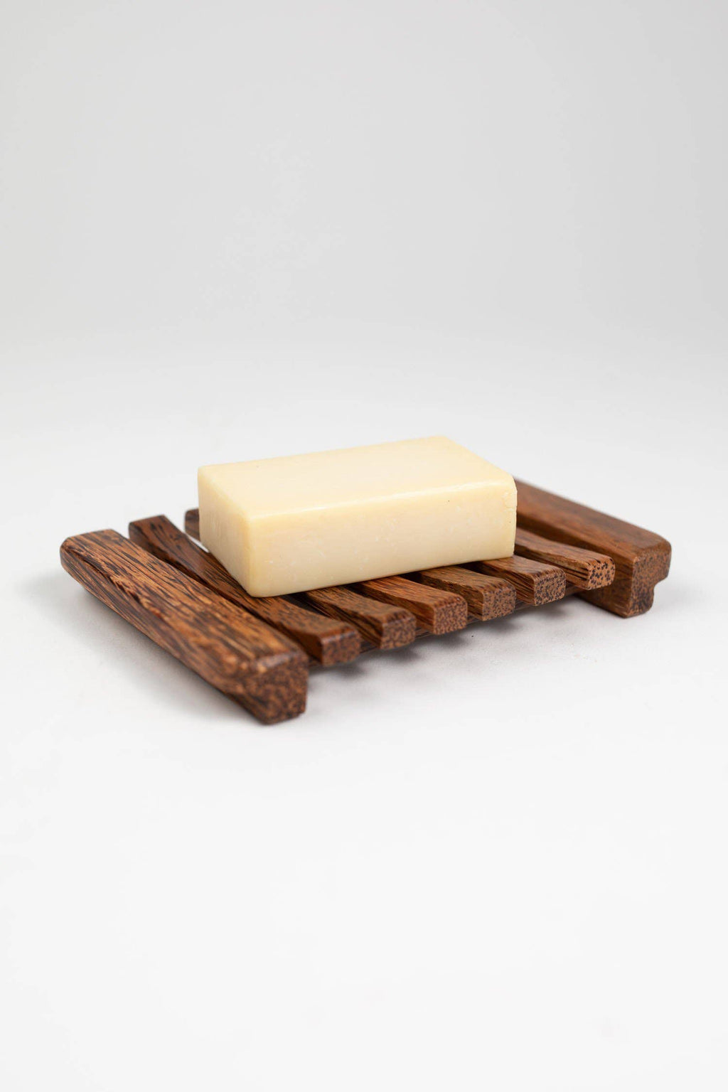 Bar of soap on a wooden soap dish against a white background