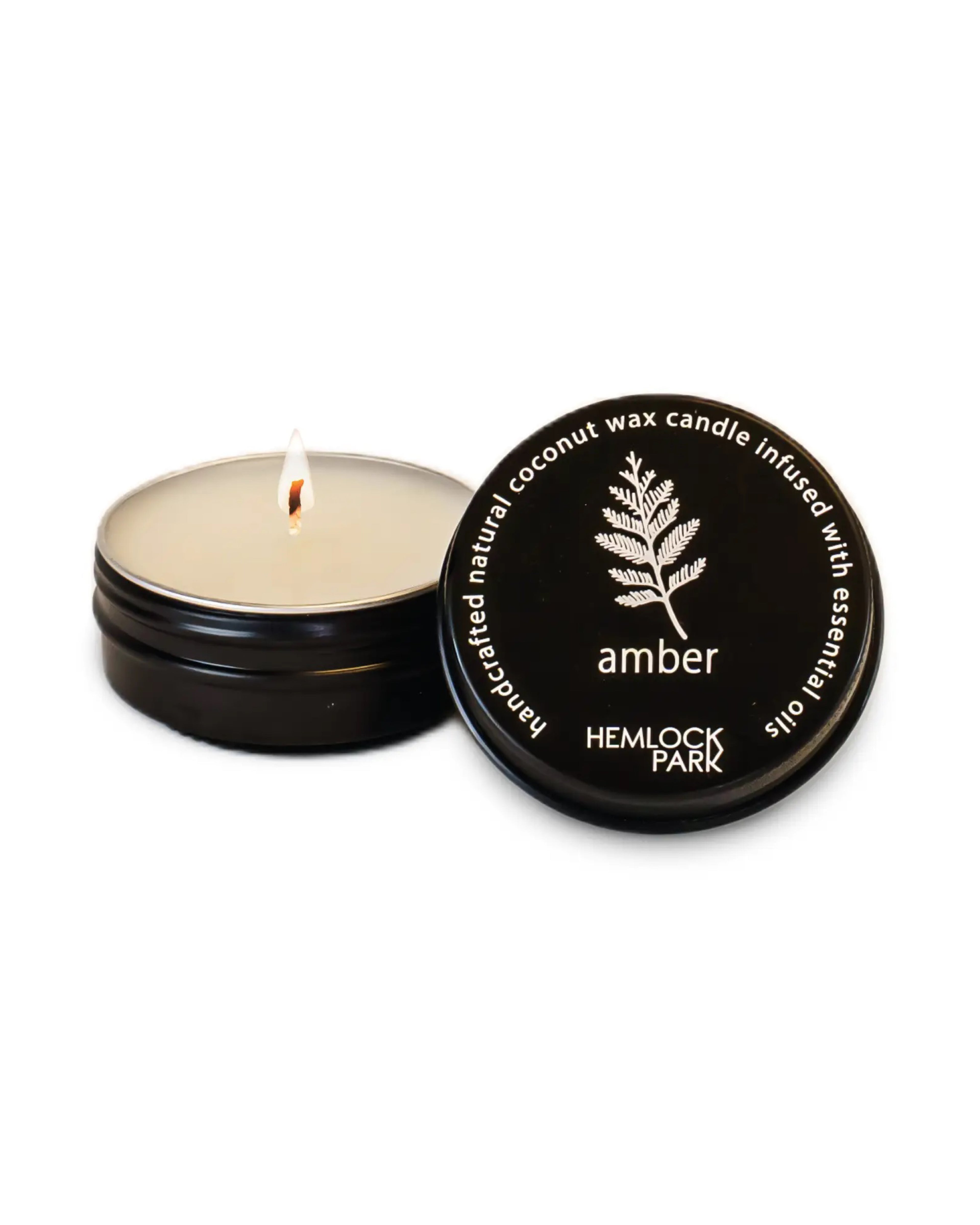 Hemlock Park candle with lit wick and black lid on a white background