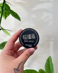 Hand holding a black candle container labeled 'palo santo' with green leaves in the background