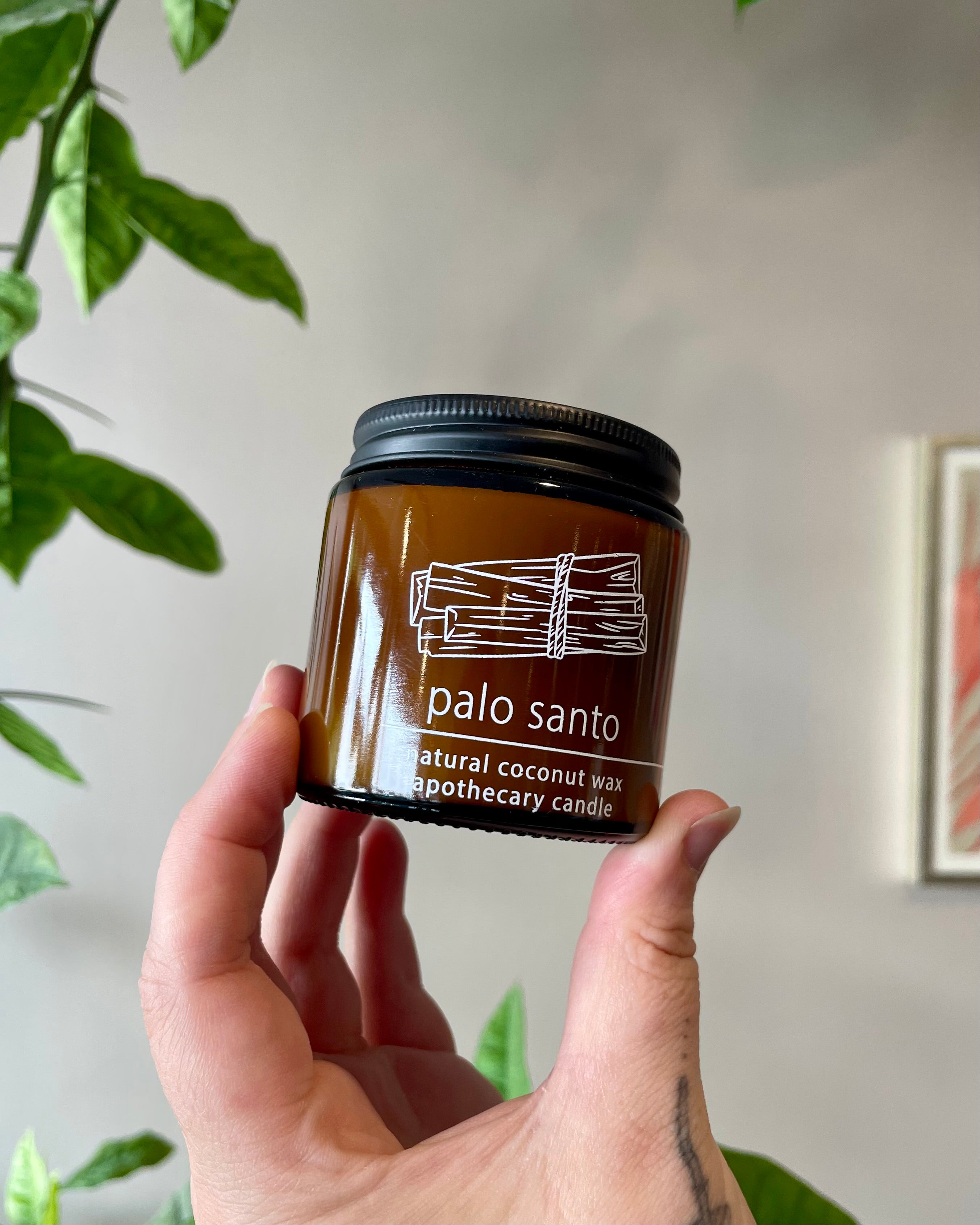 Hand holding an amber glass jar candle with a plant in the background