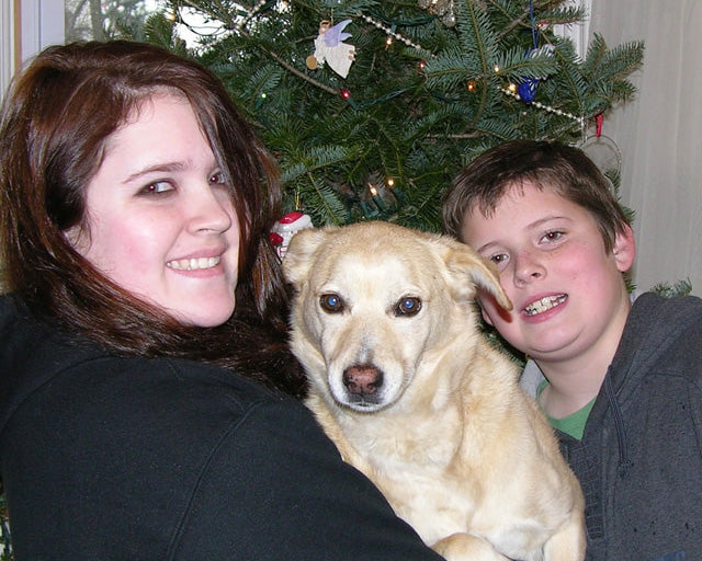 Two people with a dog in front of a decorated Christmas tree