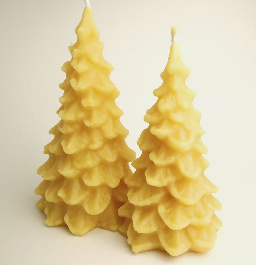Two yellow tree-shaped candles on a light beige background