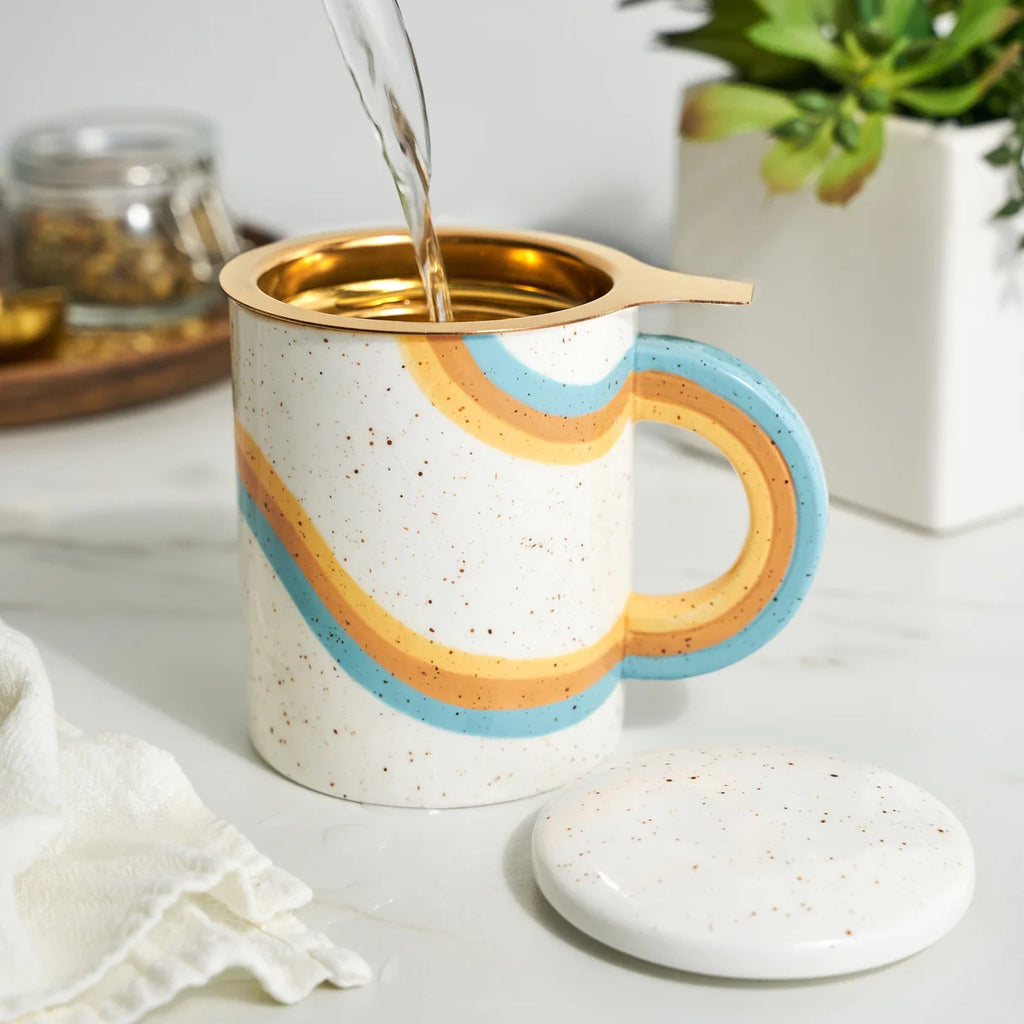 Speckled ceramic mug with rainbow design being filled with a liquid, placed on a marble surface.