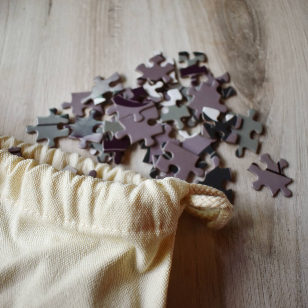 Puzzle pieces on a wooden surface with a beige drawstring bag
