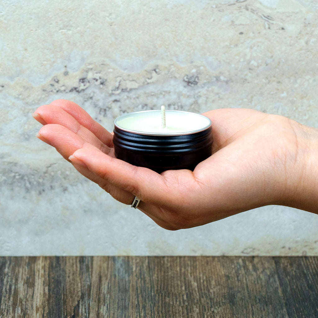 Hand holding a small black container with a candle against a neutral background