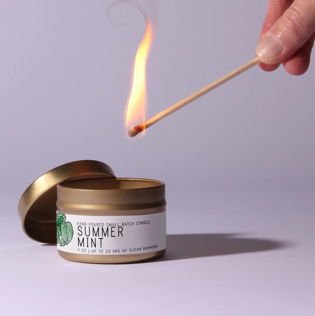 Candle labeled 'Summer Mint' being lit with a match against a plain background