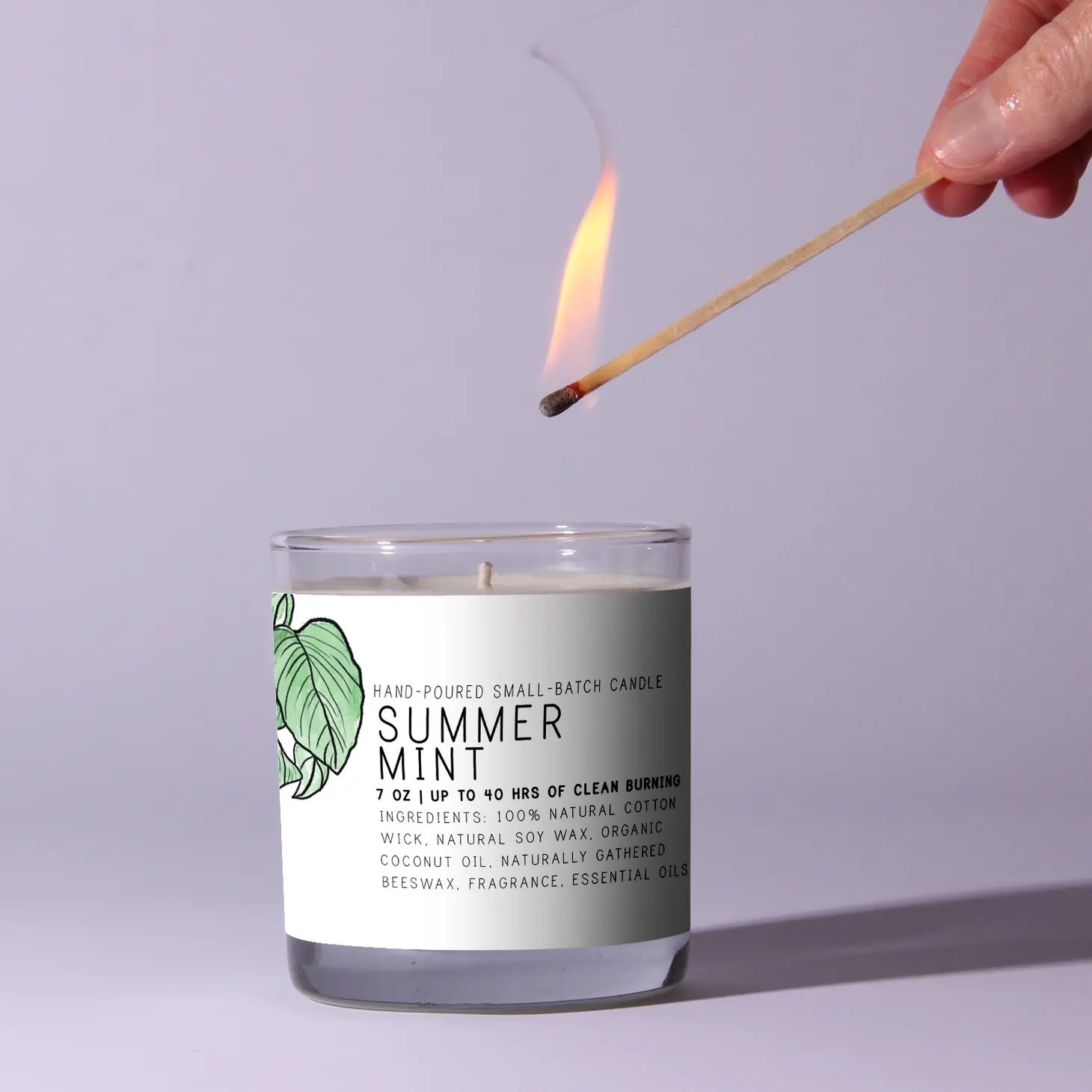 Candle labeled 'Summer Mint' being lit with a match against a light gray background