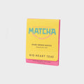Yellow and pink package of Big Heart Teas Matcha tea on a light gray background